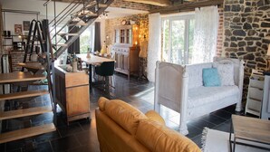 A spacious living area with a staircase, a dining table, a sofa, and a kitchen area with stone walls. - Tranquil Stay in Ardennes (Gimnée)