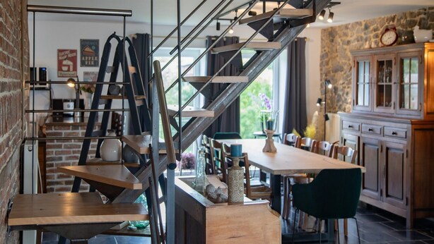 A modern kitchen with a wooden island, a staircase with metal railings, and a stone wall. - Tranquil Stay in Ardennes (Gimnée)