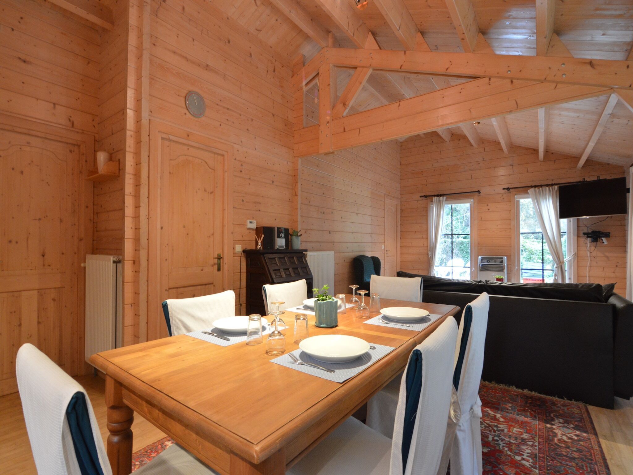 Ein Holzblockhaus-Innenraum mit einem Esstisch für vier Personen, einem schwarzen Sofa und einem an der Wand montierten Fernseher.