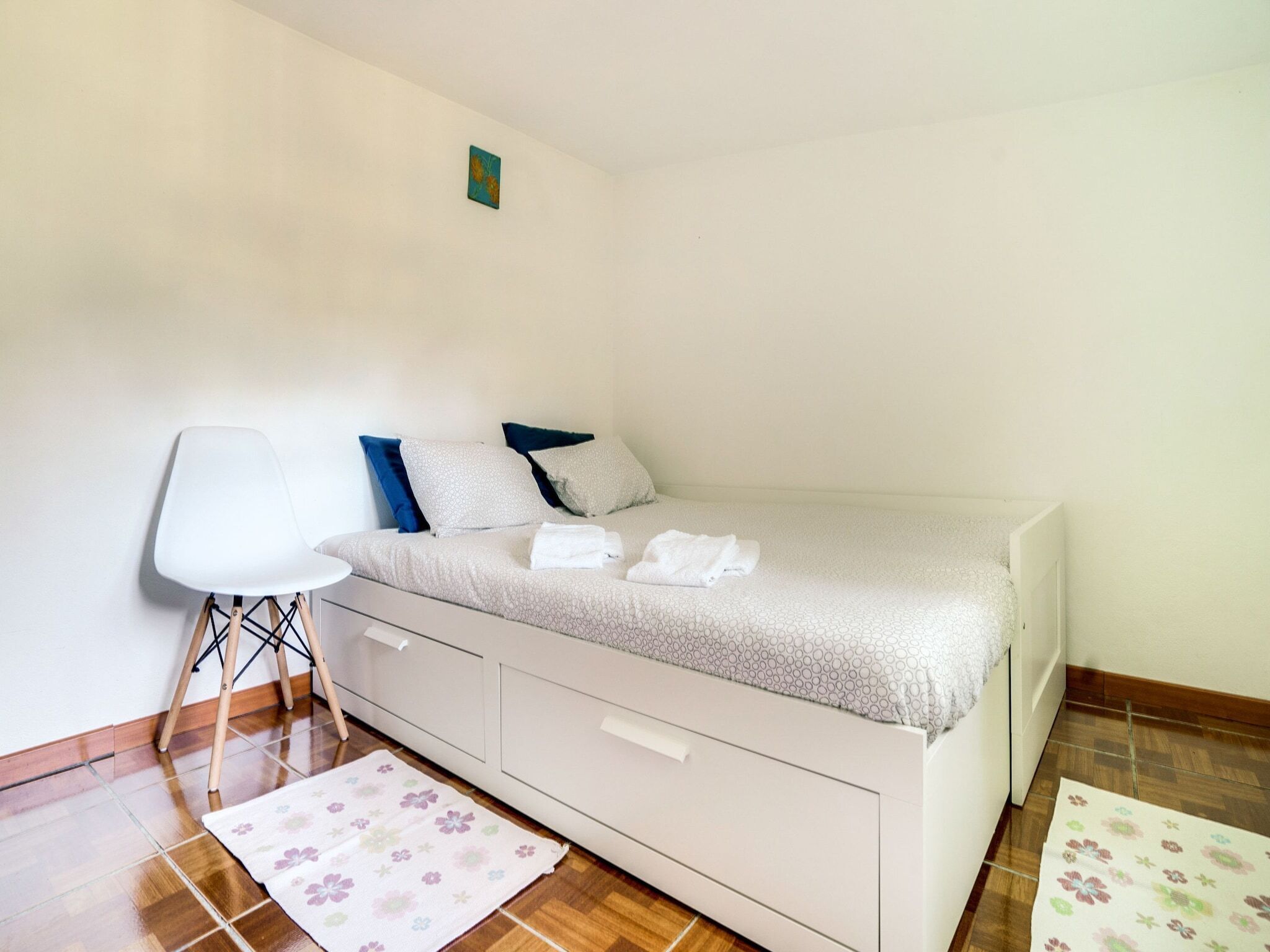 A single bed with a white headboard and drawers, a white chair, and a small table.