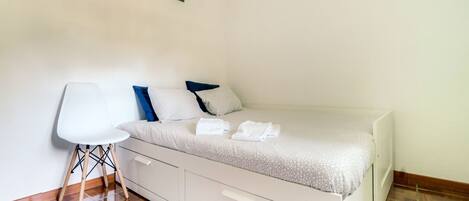 A single bed with a white headboard and drawers, a white chair, and a small table.