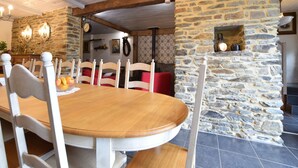 Un espace repas avec une table en bois et des chaises blanches, des murs en pierre et une cheminée en pierre.