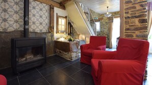 Une pièce chaleureuse avec une cheminée, des fauteuils rouges, un mur en pierre et un escalier en bois.