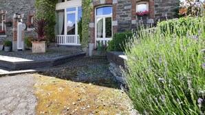 Un bâtiment en pierre avec un porche blanc, une enseigne indiquant « Hôtel-gîte », et un jardin agrémenté de lavande.