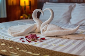 A bed with a striped pillowcase, a decorative swan towel arrangement, and a single flower. - Travellerhome Angkor (Siem Reap)
