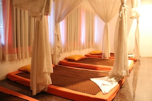 Ein Zimmer mit vier Betten, jedes mit Baldachin und orangefarbener Bettwäsche.