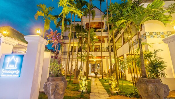A hotel entrance with a sign, palm trees, and golden statues. - Travellerhome Angkor (Siem Reap)
