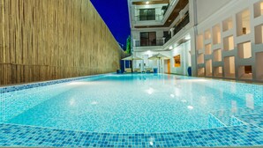 A swimming pool with blue mosaic tiles, surrounded by a wooden wall and a white building with balconies. - Travellerhome Angkor (Siem Reap)