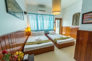 A hotel room with two beds, wooden paneling, a large window with blue curtains, and a framed Buddha statue on the wall. - Travellerhome Angkor (Siem Reap)