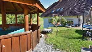 Un patio trasero con una terraza de madera, un jacuzzi, un columpio y un trampolín.
