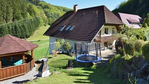 Una casa con techo inclinado, un trampolín, un columpio y una pequeña estructura de madera.