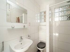Ein Badezimmer mit weißem Waschbecken, Toilette, Duschkabine aus Glas und Spiegel.