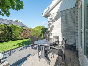 Eine Terrasse mit Tisch und Stühlen, einer Zierdeovase und einem Hecken im Hintergrund.