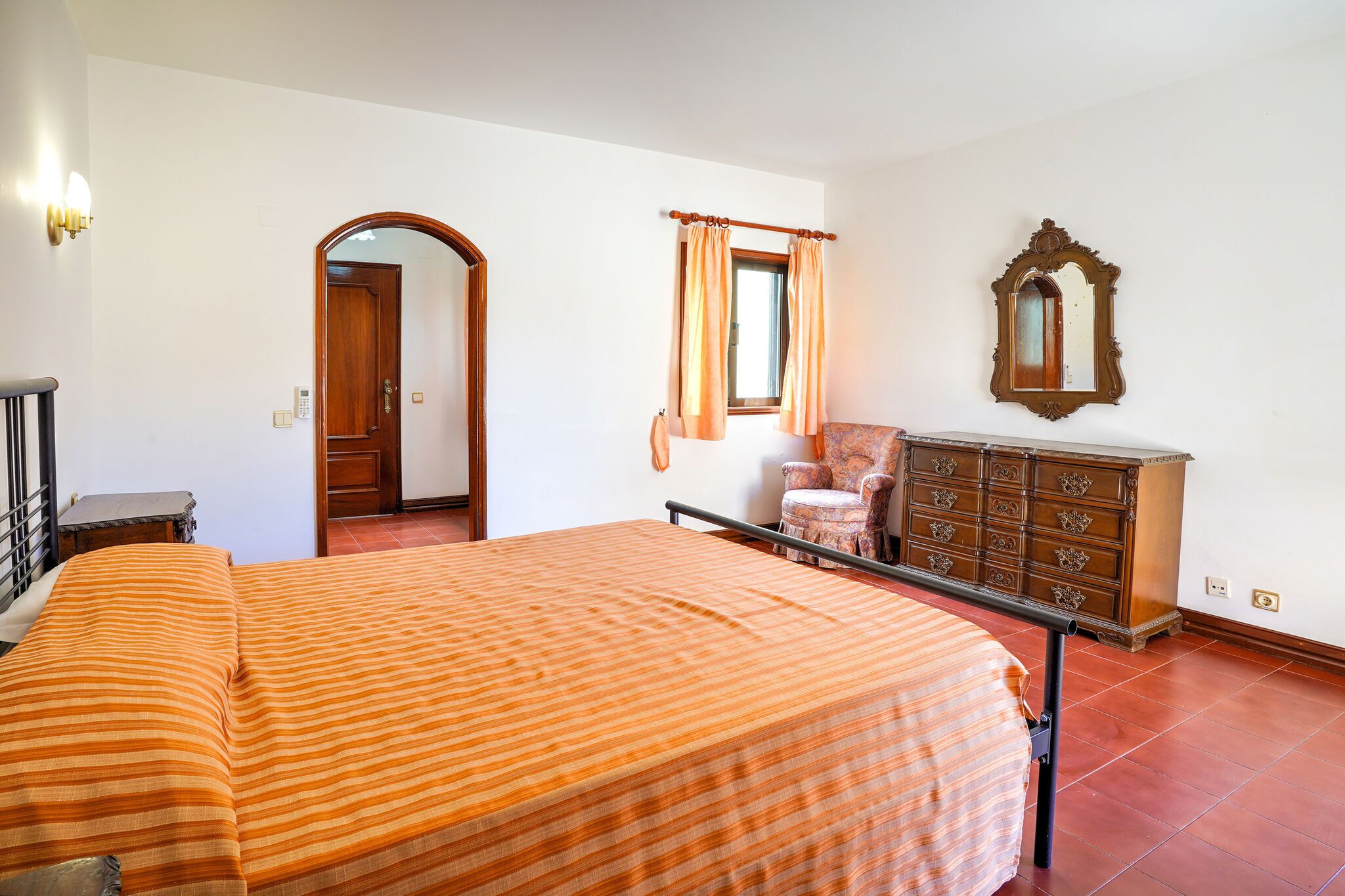 Une chambre à coucher avec un lit, une commode, une chaise, un miroir et une porte.