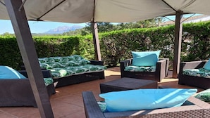 Eine Terrassensitzgelegenheit im Freien mit Korbmöbeln, einem überdachten Bereich und Blick auf Grünflächen und Berge.