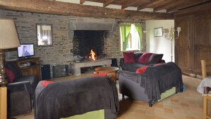 Ein rustikaler Wohnraum mit Kamin aus Stein, Holzbalken und einem Fernseher auf einem Holzständer.