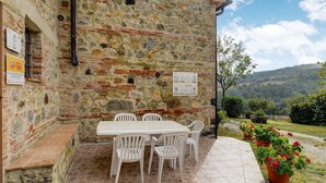 A stone building with a tiled patio, outdoor seating, and a view of a green landscape. - Belvilla by OYO Sorgente (Radicofani)