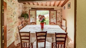 A dining room with a table set for four, wooden chairs, a vase with flowers, and a view through a door to the outside. - Belvilla by OYO Sorgente (Radicofani)