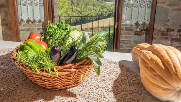 A balcony with a wicker basket of vegetables, a pumpkin, and lace curtains. - Belvilla by OYO Sorgente (Radicofani)