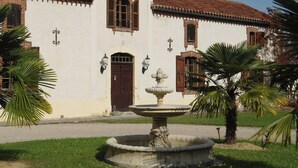 Un edificio con fachada blanca, una puerta marrón y una fuente de piedra al frente.