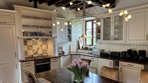 Una cocina con armarios blancos, una mesa de comedor de madera con sillas, un jarrón de flores y una lámpara de diseño.