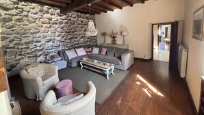 Una sala de estar con pared de piedra, vigas de madera en el techo, un sofá gris, una mesa de centro y una lámpara.