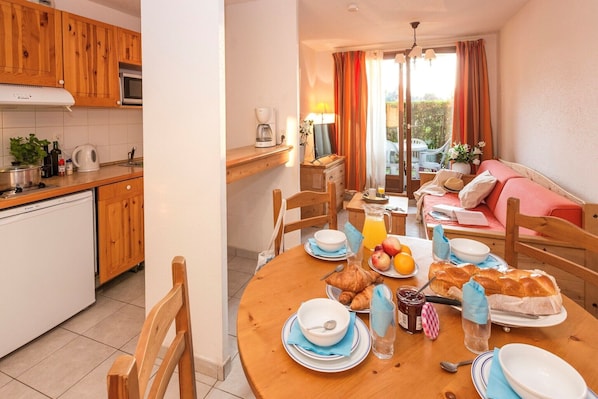 A cozy kitchen with wooden cabinets, a dining area with a table set for breakfast, and a view of the outdoors through a window.