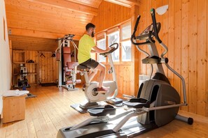 A person using an elliptical trainer in a room with wooden walls and a wooden floor. - Apartment near Lake Geneva (Bernex)