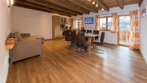 Un vaste espace de vie doté d’un plafond en bois, d’une table à manger avec des chaises, d’un canapé et d’une cuisine à l’arrière-plan.