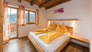Une chambre avec un plafond en bois, un lit avec des oreillers jaunes, une fenêtre avec des rideaux et une vue sur les montagnes.