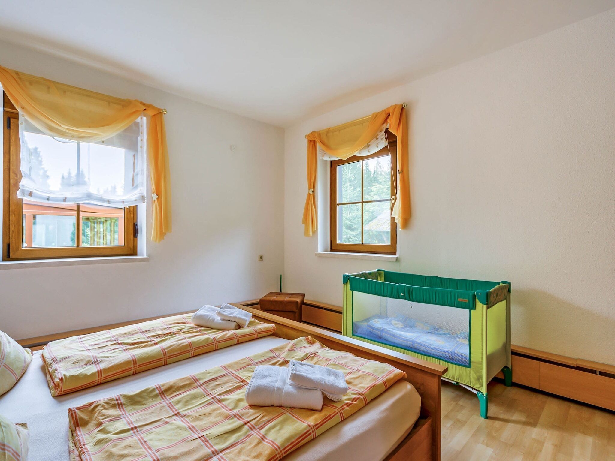 Une chambre avec deux lits, un berceau et deux fenêtres avec des rideaux.