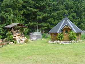 Eine rustikale Holzhütte mit Holztür und Schornstein, umgeben von einer Wiese und dichtem Wald.