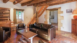 Un interior rústico con vigas de madera a la vista, un sofá de cuero, una mesa de madera y una escalera que sube a un nivel superior.