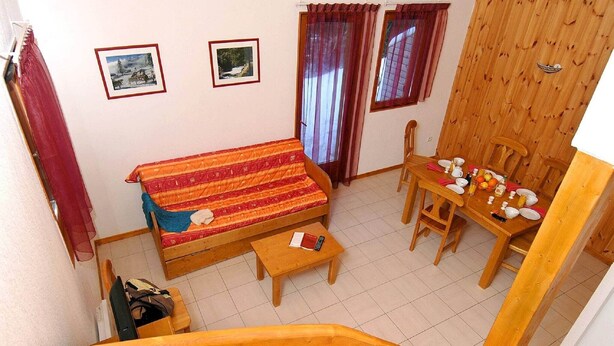A furnished room with a sofa, a dining table set for two, and a staircase. - Chalet in France near Ski Slopes (Le Dévoluy)