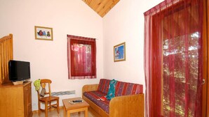 A living room with a sofa, a wooden table, a television, and two windows with curtains. - Chalet in France near Ski Slopes (Le Dévoluy)