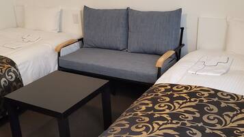 Ett hotellrum med två separata sängar, en grå soffa, ett litet bord och ett mönstrat överkast.