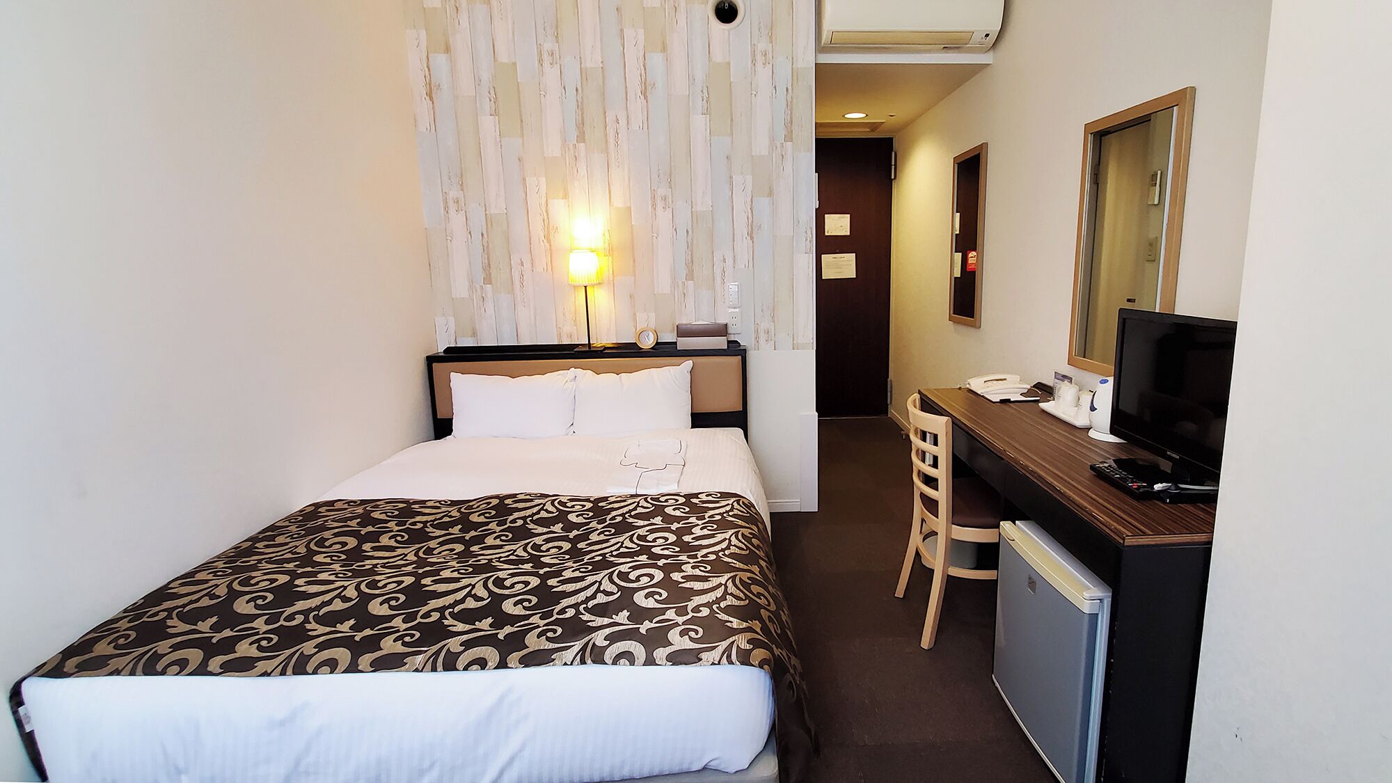 Ein Hotelzimmer mit Bett, Schreibtisch, Stuhl, Fernseher und Spiegel.