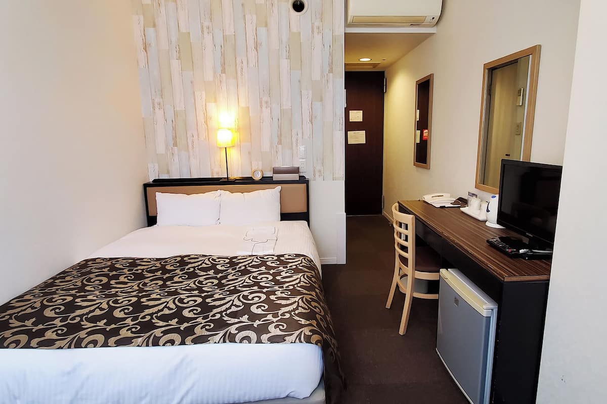 A hotel room with a bed, desk, chair, television, and a mirror.