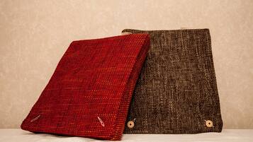 Due cuscini con tessuto sagomato, uno rosso e uno marrone, su una superficie bianca su sfondo beige.