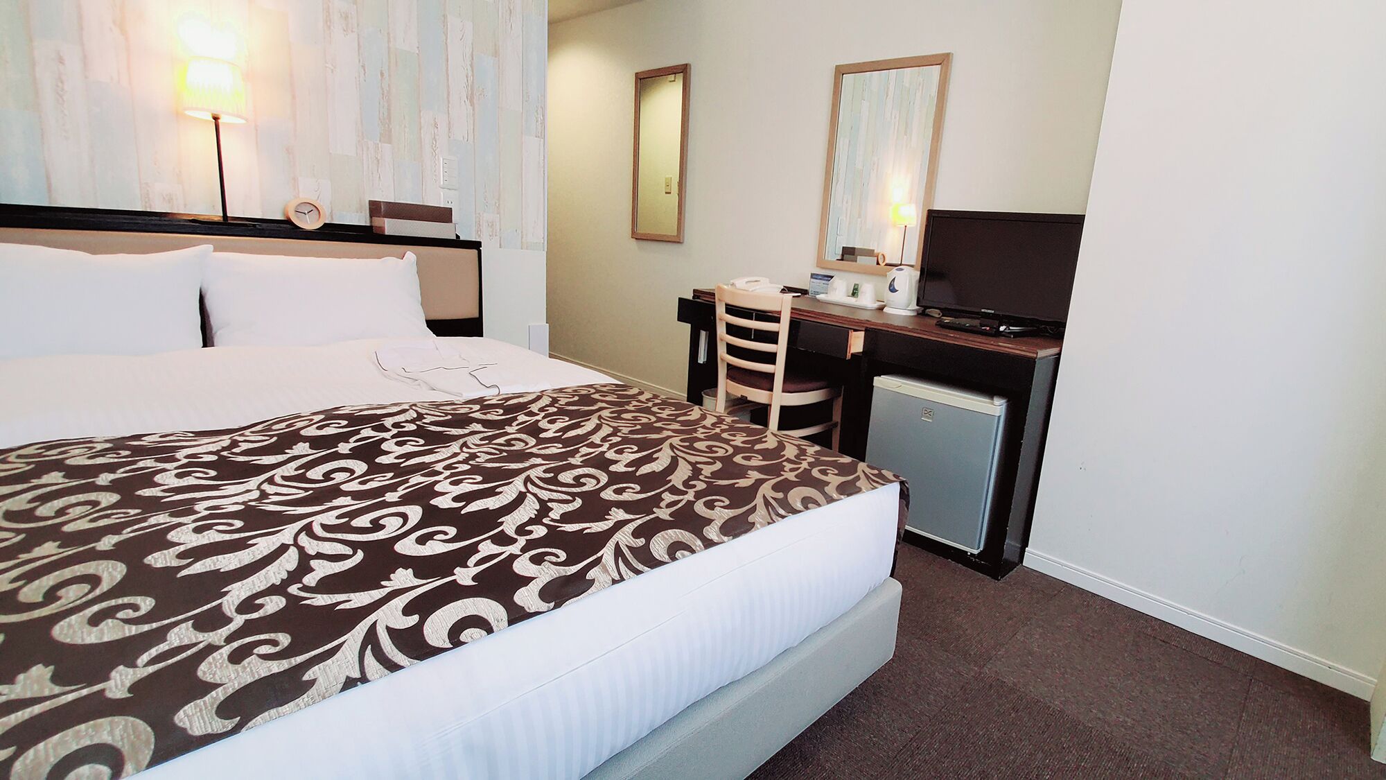 Ein Hotelzimmer mit einem großen Bett, einem Schreibtisch mit Computer, einem Fernseher und einem kleinen Kühlschrank.