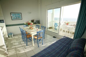 A room with a dining table, chairs, a sofa, and a view of the sea through large windows. - Apartment in France with Ocean Views (Fouras)