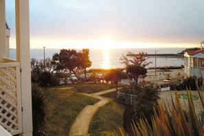 A coastal view with a sunset, a pathway leading to a seating area, and a building with a balcony.