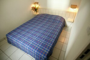 A single bed with a blue and red plaid bedspread in a room with white walls and a white headboard.