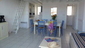 A dining area with a white table, blue chairs, and a ladder leading to an upper level. - Apartment in France with Ocean Views (Fouras)