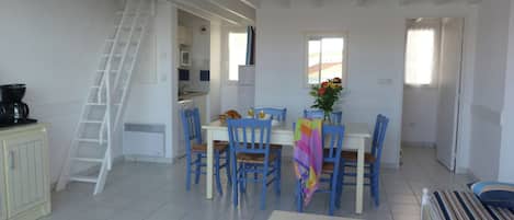 A dining area with a white table, blue chairs, and a ladder leading to an upper level.