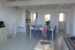 A dining area with a white table, blue chairs, and a ladder leading to an upper level. - Apartment in France with Ocean Views (Fouras)