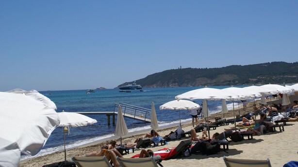 Una playa con tumbonas y sombrillas, un muelle y barcos en el agua.
