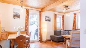 A cozy room with a wooden ceiling, a dining table with chairs, a sofa, and a window with curtains.