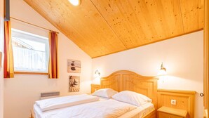 A bedroom with a wooden bed, two bedside tables, a nightstand, a window with curtains, and wall art.