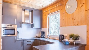 A modern kitchen with grey cabinets, a built-in oven, a coffee maker, and a window with a view of trees.